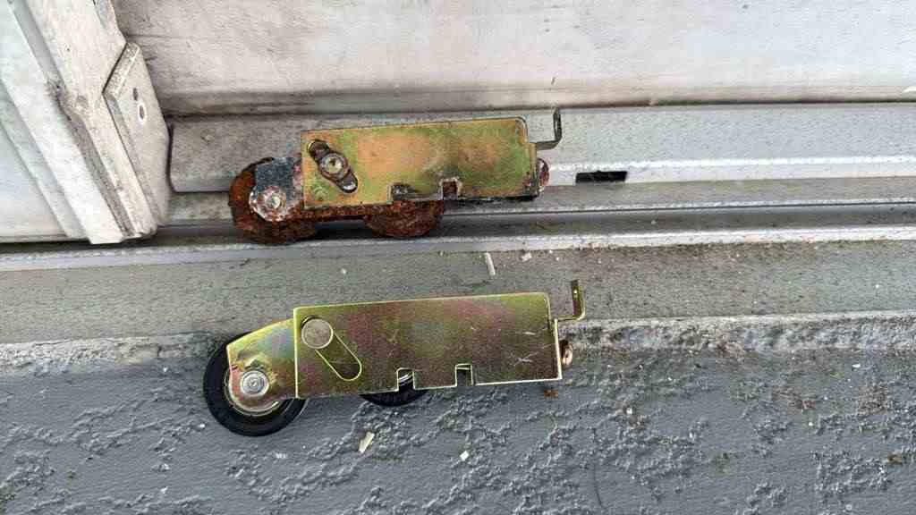 Worn sliding door roller next to a new replacement roller